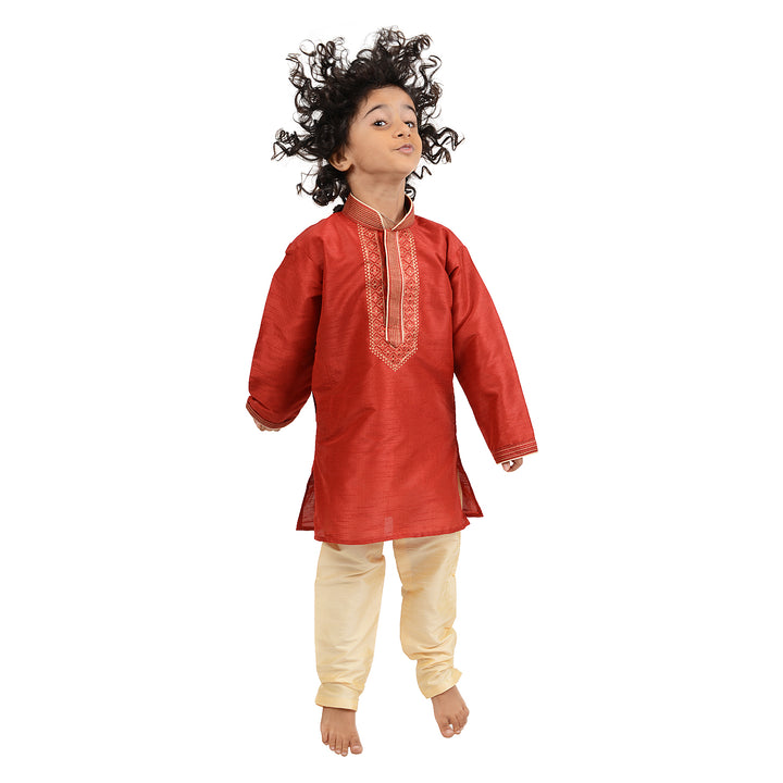 Jumping child in Kids Gold Kurta Set showcasing red art silk kurta with gold embroidery and cream churidar, ideal for festive occasions.
