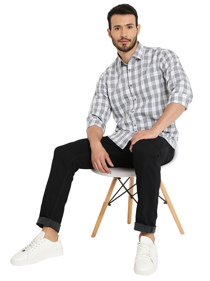 Model seated wearing grey slim fit checked shirt with black pants and white sneakers, styled for a relaxed casual look.