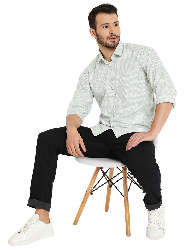 Model seated wearing green slim fit shirt with small checks, paired with black jeans and white sneakers for a smart-casual outfit.